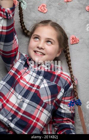 Portrait d'une jolie fille souriante et charmante avec des picots amusants sur un tapis gris avec des biscuits doux au coeur. Concept de Saint-Valentin ou d'anniversaire Banque D'Images