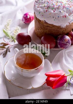 Bon petit déjeuner de Pâques encore la vie avec une tasse de thé en porcelaine blanche, des œufs de couleur et un gâteau de Pâques. Banque D'Images