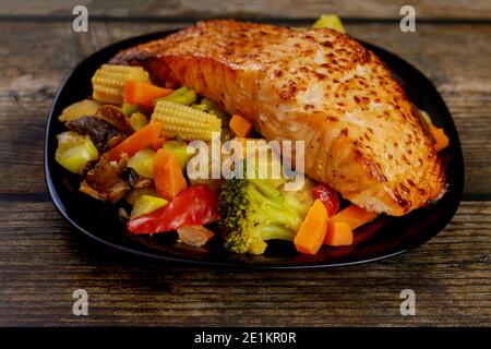 Un morceau de saumon cuit avec des légumes asiatiques sautés sur une assiette noire. Gros plan. Banque D'Images