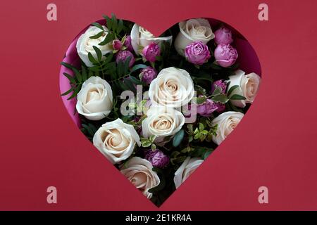 Trou dans le papier couleur vin en forme de coeur à travers les fleurs et les feuilles sont visibles. Concept de bonne Saint Valentin Banque D'Images