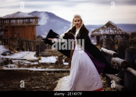 Magnifique viking blond habillé d'un manteau noir sur fond de château. Beau décor de film - un ancien village viking Banque D'Images