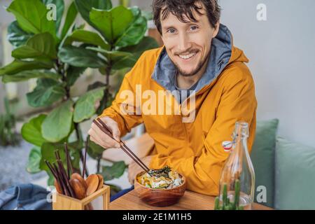 Homme mangeant le bol de poke biologique cru avec du riz et des légumes gros plan sur la table. Vue de dessus horizontale Banque D'Images