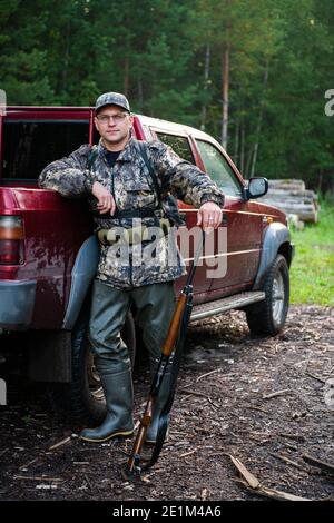 Homme chasseur debout avec fusil de chasse près de sa voiture en plein air préparation à la chasse aux oiseaux dans la forêt d'automne Banque D'Images