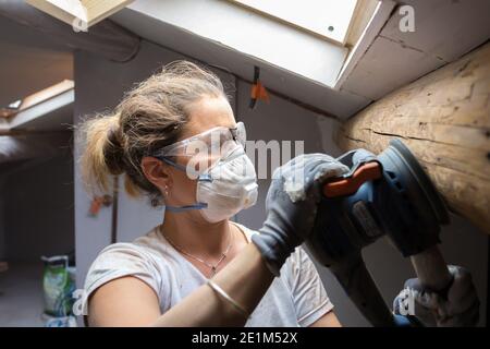 Femme rénovant la maison d'Attic - poutre abrasive Banque D'Images