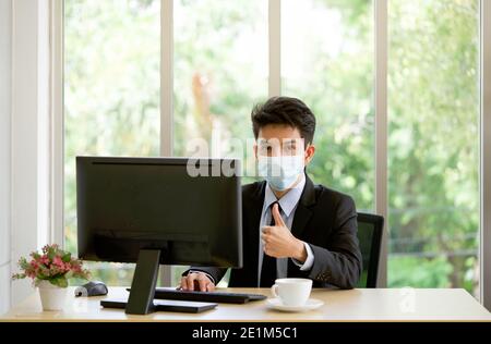 Les jeunes hommes d'affaires asiatiques portent un masque lorsqu'ils travaillent au bureau. Se protéger contre la propagation des maladies infectieuses du coronavirus 2019 Banque D'Images