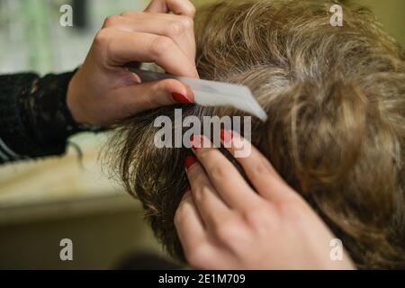 Coiffeur de cheveux fille tout en appliquant la teinture de cheveux à un blanc femme âgée aux cheveux client au travail, soins de beauté à la maison Banque D'Images