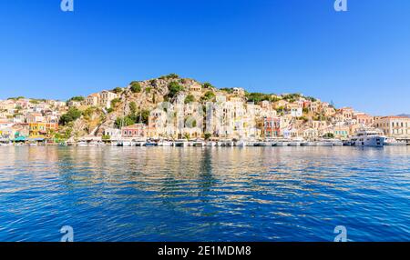 Symi, Grèce, les demeures néoclassiques surplombent les bateaux amarrés le long du pittoresque port riverain de Gialos Town, Symi Island, Dodécanèse, Grèce Banque D'Images