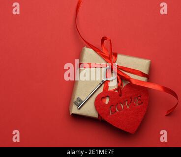 boîte carrée avec noeud en soie rouge et coeur en tissu sur fond rouge, vue du dessus, jour de la saint-valentin Banque D'Images