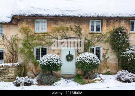 Chalet en pierre de Cotswold avec couronne de noël dans la neige de décembre. Taynton, Cotswolds, Oxfordshire, Angleterre Banque D'Images