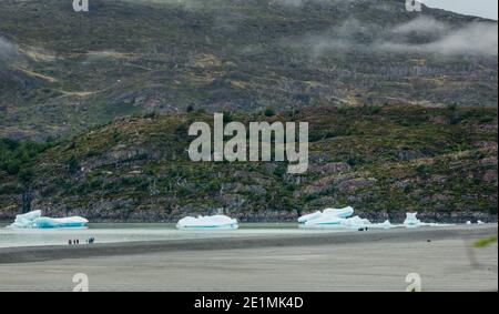 Les touristes sur une rive de moraine sont éclipsés par de grandes icebergs vêtus de Glacier Grey, bloqués au parc national Torres del Paine, Patagonie, Chili Banque D'Images