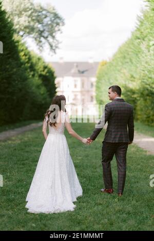 Jeune couple de mariage élégant posant joyeusement sur l'allée avec la toile de fond du palais. Banque D'Images