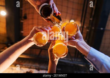 Vue de dessous de quatre amis faisant un toast avec de la bière. Intérieur pub. Banque D'Images