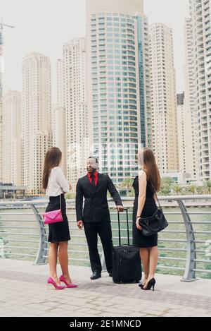 Trois hommes d'affaires se tenant à Dubai Marine et discutant des plans d'affaires pour le mois prochain. Un homme afro-américain et deux femmes européennes en costume Banque D'Images