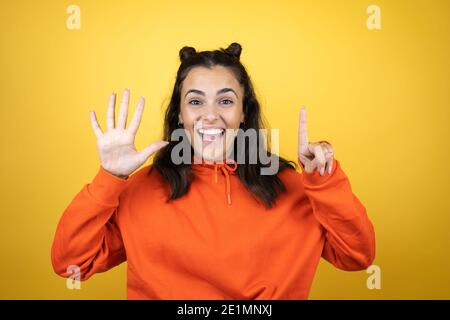 Jeune belle femme portant un sweat-shirt sur fond jaune isolé montrant et en pointant vers le haut avec les doigts numéro six tout en souriant confiant et h Banque D'Images