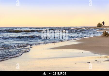 les basses vagues roulent sur la côte sablonneuse, dans la distance qu'une personne porte quelque chose, foyer sélectif Banque D'Images