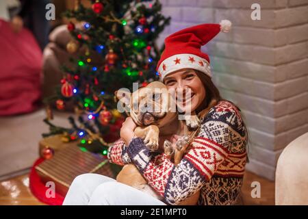 Gros plan sur une jeune femme qui embrasse son animal de compagnie. En arrière-plan arbre de Noël et cadeaux. Concept des fêtes de Noël. Banque D'Images