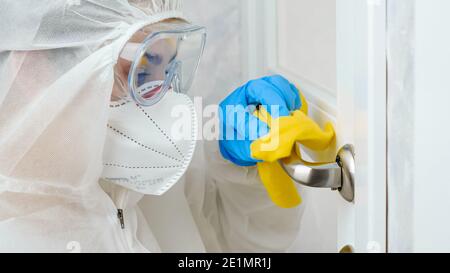 Portrait d'une femme en costume de protection, masque médical et gants dessinant et nettoyant les poignées de porte à l'hôpital. Nettoyage de la maison contre les virus et Banque D'Images