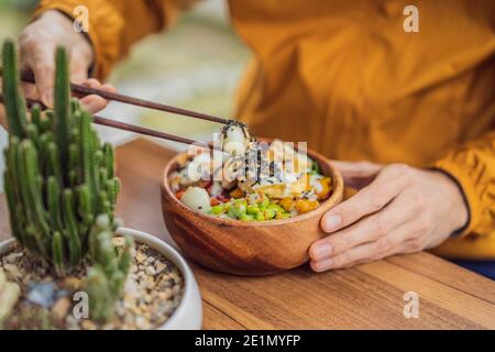 Homme mangeant le bol de poke biologique cru avec du riz et des légumes gros plan sur la table. Vue de dessus horizontale Banque D'Images