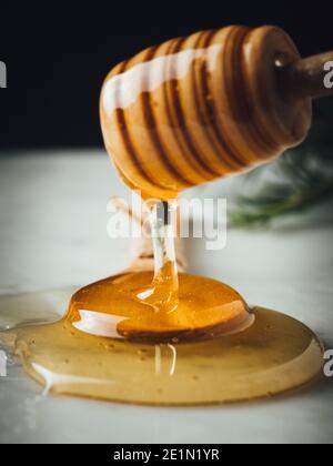 Flux de miel. Le miel doré, jaune, cru est en train de tomber de la louche de miel sur une cuillère à soupe de bois. Ingrédient sucré sain pour les cosmétiques naturels, les pâtisseries et Banque D'Images