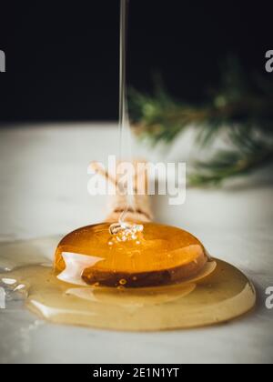 Flux de miel. Le miel doré, jaune, cru est en train de tomber de la louche de miel sur une cuillère à soupe de bois. Ingrédient sucré sain pour les cosmétiques naturels, les pâtisseries et Banque D'Images