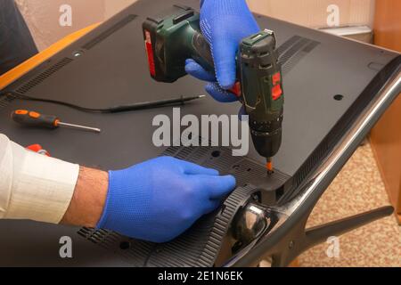 Réparation du téléviseur LCD dans le centre de service. Un technicien retire le panneau arrière à l'aide d'un tournevis électrique. Mise au point sélective, gros plan. Banque D'Images