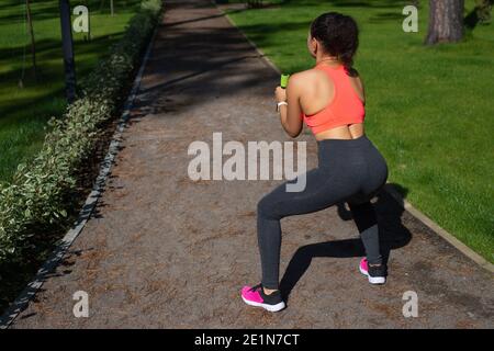 Vue depuis l'arrière d'une jeune femme sportive haltères sur une voie de course dans le parc urbain Banque D'Images