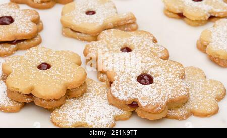 Biscuits sablés en forme de fleur remplis de confiture de framboises. Petits gâteaux frais gros plan sur fond blanc Banque D'Images