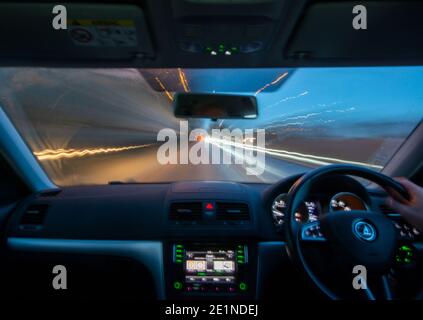 Vue longue exposition depuis l'intérieur d'une voiture roulant le long d'une route à l'aube avec des sentiers légers de la circulation venant en sens inverse Banque D'Images