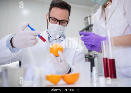 Le technologue injecte du liquide dans l'orange tandis que l'assistant l'aide. Banque D'Images