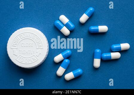 Capsules bleues et blanches déversées d'une bouteille Banque D'Images