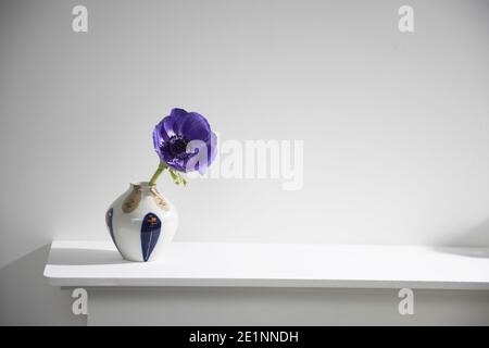 Une anémone bleue dans un vase multicolore dans le style des années 70 sur la table avec des livres comme décoration intérieure. Copier l'espace Banque D'Images