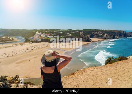 Une femme avec un chapeau sur sa tête, sur la rive, admire la vue de la plage portugaise, Odeceixe. Banque D'Images