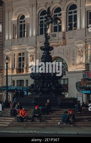 Londres, Royaume-Uni - 19 novembre 2020 : peu de personnes assises sur les marches de la statue d'Eros à Piccadilly Circus, l'un des plus populaires et généralement très occupé t Banque D'Images