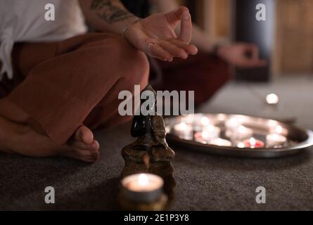 Femme anonyme méditant près de la statuette de Bouddha et des bougies dans l'obscurité studio Banque D'Images