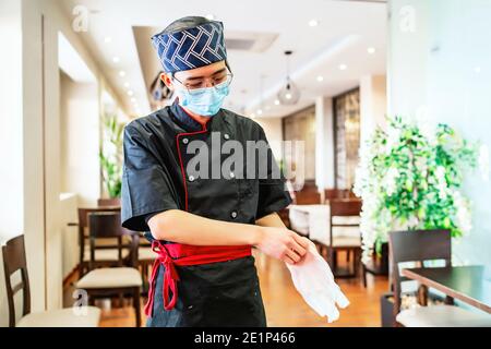 Chef japonais expert en sushi mettant des gants Banque D'Images