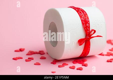 Rouleau de papier toilette en cadeau pour la Saint-Valentin, à côté de coeurs rouges sur fond rose. Copier l'espace Banque D'Images