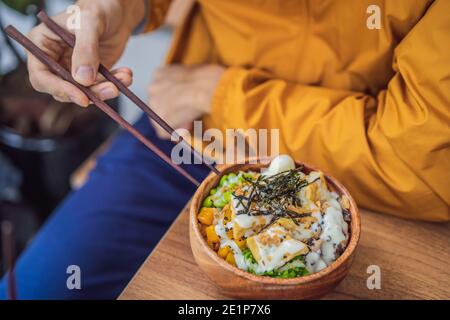 Homme mangeant le bol de poke biologique cru avec du riz et des légumes gros plan sur la table. Vue de dessus horizontale Banque D'Images