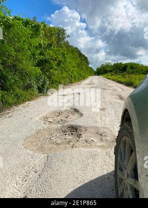 Route brisée pleine de trous de pot avec la voiture dedans conduite avant dangereuse Banque D'Images