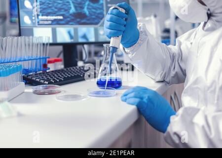 Médecin travaillant pour trouver un remède pour le coronavirus à l'aide d'une micropipette et d'une boîte de Petri portant un vêtement de protection et un masque facial. Chimiste en laboratoire moderne faisant des recherches en utilisant le distributeur pendant l'épidémie mondiale avec Covid-19. Banque D'Images