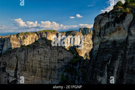 Vue en soirée sur le paysage typique des Météores. Roches sédimentaires, falaises, piliers de grès. Ciel bleu et grands nuages. Grèce, Patrimoine mondial de l'UNESCO Banque D'Images