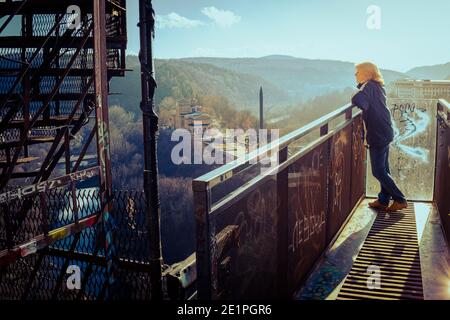 Femme sur une plate-forme de passerelle surélevée surplombant le monument d'Assens et la rivière Yantra dans la ville de Veliko Tarnovo le jour de l'hiver du nouvel an. Banque D'Images