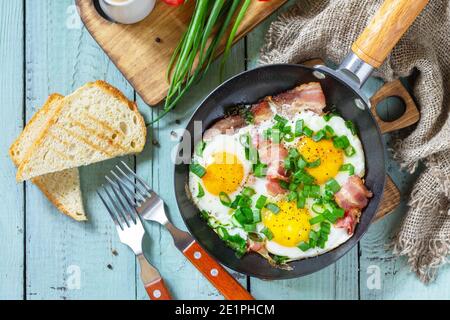 Œufs brouillés de printemps avec oignons verts et bacon dans une poêle en fonte sur fond de bois rustique. Plan d'étapage avec vue de dessus. Banque D'Images
