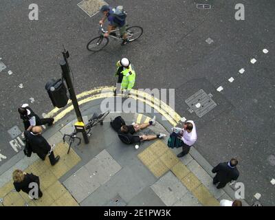 Accident de vélo, cycliste couché sur la chaussée avec un policier et un témoin, après un accident sur City of London Street. Banque D'Images