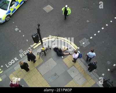 Accident de vélo, cycliste couché sur la chaussée avec un policier et un témoin, après un accident sur City of London Street. Banque D'Images