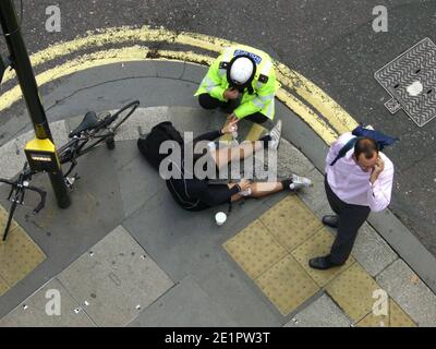 Accident de vélo, cycliste couché sur la chaussée avec un policier et un témoin, après un accident sur City of London Street. Banque D'Images