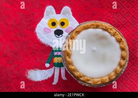 Tarte aux pommes de terre hachée glacée de Sainsburys sur une serviette de Noël festive - pâtisseries fourrées de viande hachée, recouvertes de glaçage blanc doux Banque D'Images