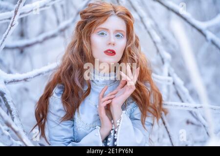 Une jeune femme à tête rouge, une princesse, marche dans une forêt d'hiver en robe bleue. Banque D'Images