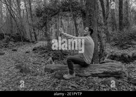 Homme de mode prenant un selfie sur téléphone cellulaire dans beau Forest.Male utilisant un smartphone, concept de technologie d'extérieur style de vie.Photographie noir et blanc Banque D'Images