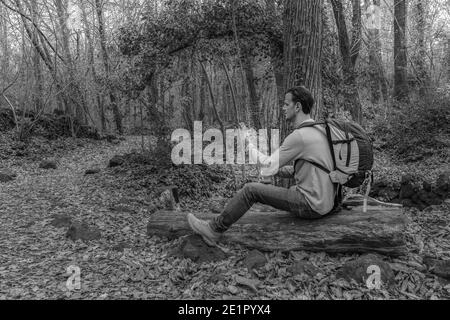 Homme utilisant un smartphone assis avec un sac à dos sur un arbre Dans la forêt.style de vie de randerlust.Travel Wanderlust concept.couleurs noir et blanc avec Banque D'Images