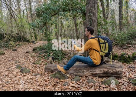 Homme utilisant un smartphone assis avec un sac à dos sur un arbre en forêt.concept de voyage, marche, l'excursion, randonneur style de vie extérieur.espace de copie . Banque D'Images